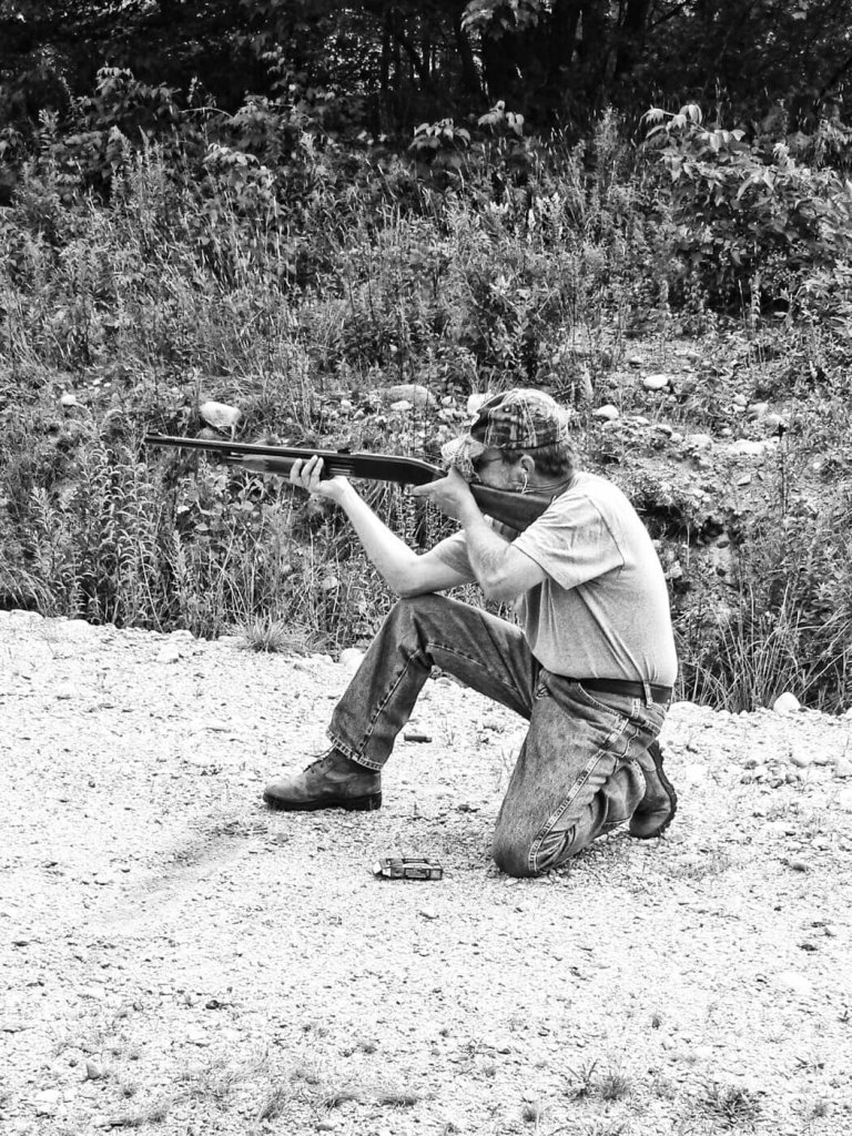 Man firing shotgun while kneeling