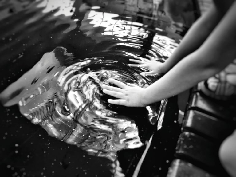 black and white photo of hands touching water