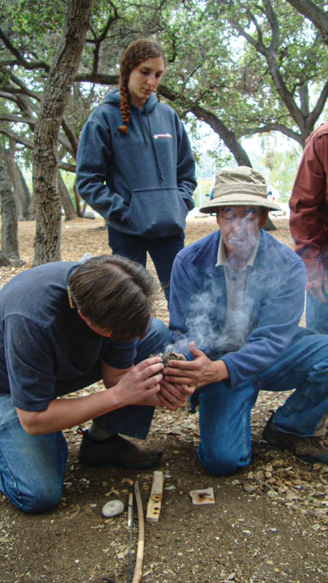 Gary Gonzales (right) instructs students how to carefully coax an ember into a flame.