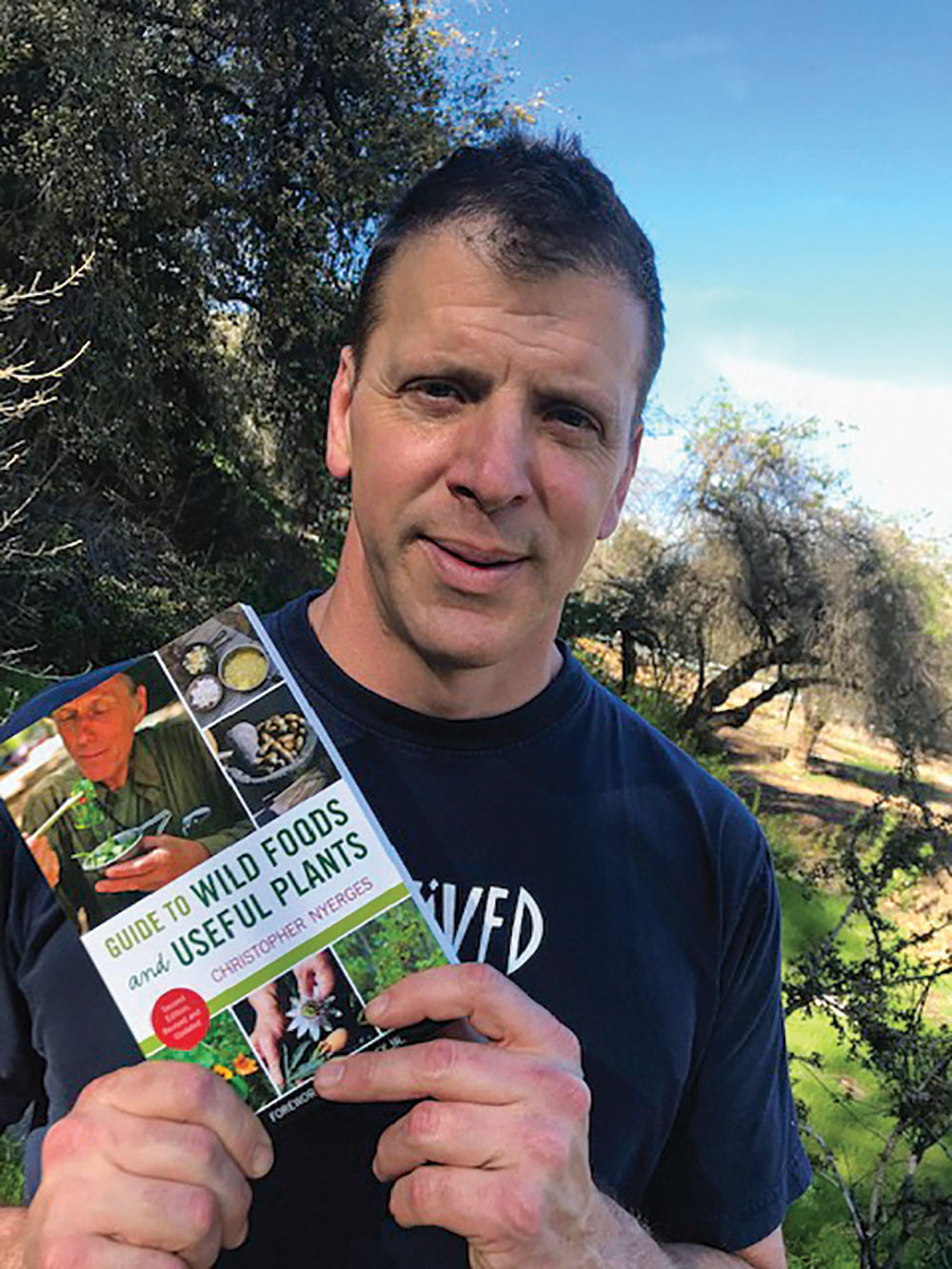 Roger Moore holds a copy of author Nyerges’ book about wild plants that are found all over the United States