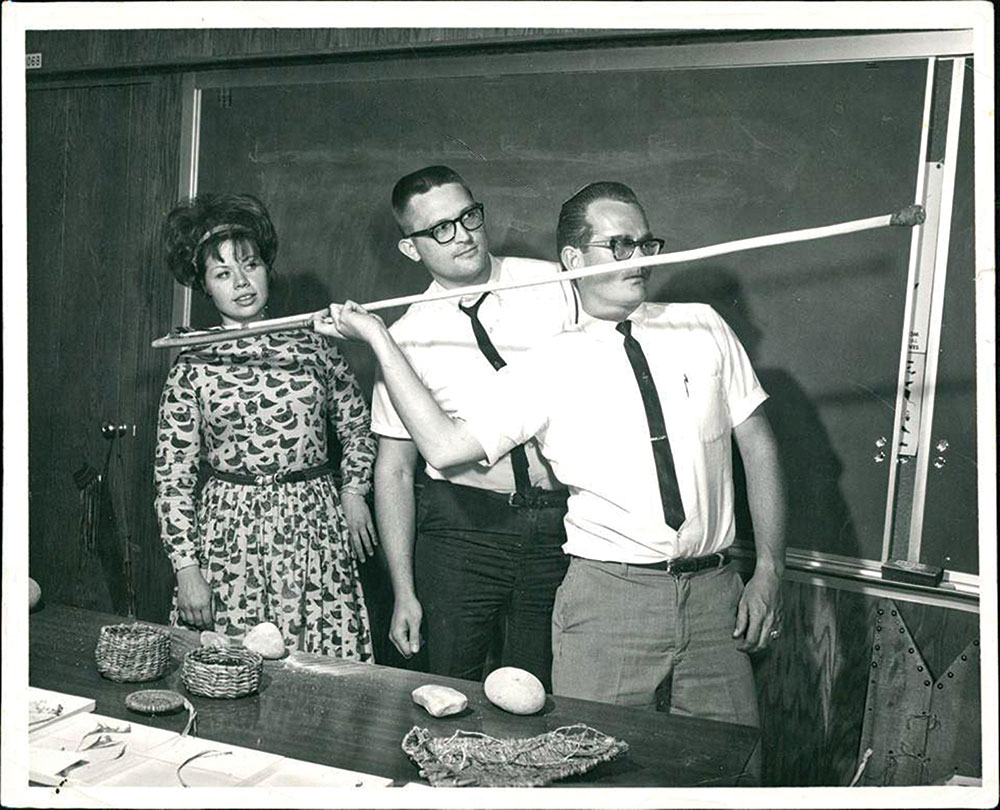 Olsen (right) demonstrates an atlatl in his Brigham Young University classroom, circa 1967